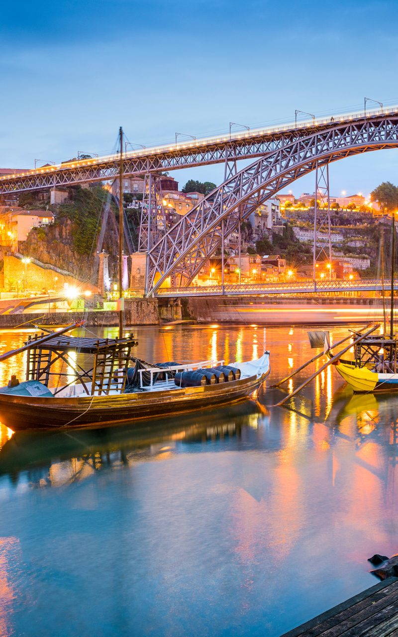 Wooden rabelo boats moored on the Douro river in Porto at blue hour, the Dom Luis bridge lit above them